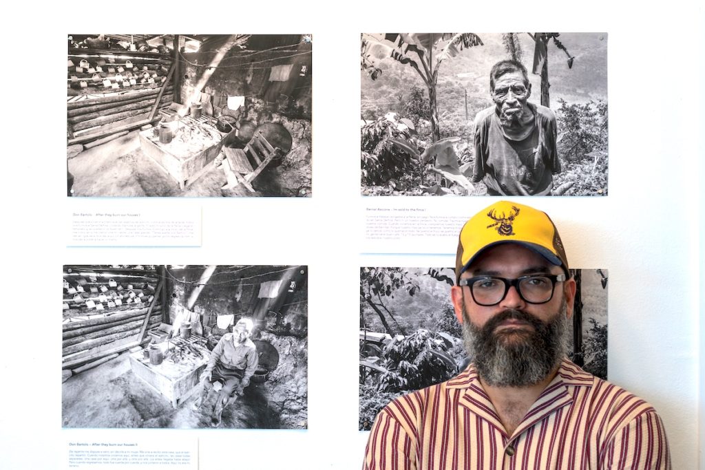 Photograph of Alejandro Flores in front of an exhibition of his photographs.