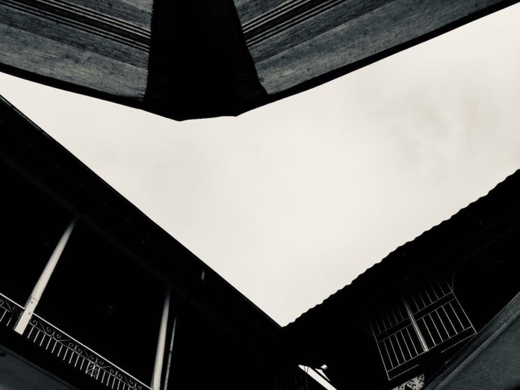 Monochrome photography looking up towards the sky through angular roof tops.